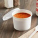 A white Choice paper food cup filled with soup and a vented plastic lid on a table.