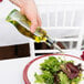 A hand pouring Tablecraft olive oil into a salad on a plate of green and red leaves.