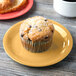 A muffin on a GET Tropical Yellow melamine plate next to a cup of coffee.