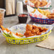A yellow oval plastic fast food basket filled with chicken wings and fries on a table in a family-style restaurant.