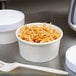 A bowl of noodles next to a white Choice paper food container with a fork.