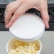 A person's hand holding a Choice white vented lid over a container of pasta.
