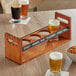 An Acopa walnut finish wooden beer flight rack with glasses of beer on a table.