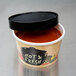 A black cylinder containing Choice paper soup cup with black lid filled with hot sauce.