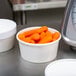 A bowl of baby carrots next to a scale on a counter.