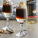A close-up of two glasses of brown liquid with whipped cream and nuts next to a bottle of DaVinci Gourmet Classic Hazelnut Flavoring Syrup.