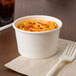 A Choice white paper food cup filled with spaghetti and meat sauce with a fork.