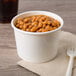 A close up of a Choice white paper food cup filled with beans on a table with a fork.