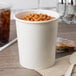 A white Choice paper food cup filled with beans on a table with a spoon.