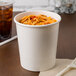 A white paper food cup filled with noodles on a table.