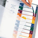 A hand opening a binder with colorful file folders labeled with Avery Ready Index dividers.