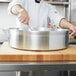 A chef stirring a large silver Vollrath Wear-Ever brazier pan.