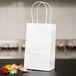 A Duro white paper bag with handles holding a few candies.