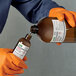 A person in orange gloves pouring liquid into a brown bottle using Avery UltraDuty GHS labels.