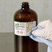 A gloved hand using an Avery UltraDuty label to wipe a brown bottle of chemicals.