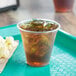 A clear PET plastic cup filled with iced tea on a tray with popcorn.