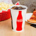 A Solo Coke paper cold cup filled with soda on a table with pizza.