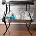 A Tablecraft stainless steel beverage tub on a metal cart filled with glasses and a bottle.