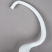 A white curved KitchenAid dough hook on a gray surface.