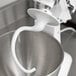 A KitchenAid dough hook with a white handle on a silver stand mixer bowl.