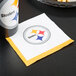 A Pittsburgh Steelers 2-ply beverage napkin with the team logo on a table with a drink.