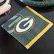 A Creative Converting Green Bay Packers beverage napkin in plastic wrap with a green and yellow design.
