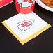 A Kansas City Chiefs beverage napkin with a logo on it next to a plate of food.