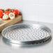 An American Metalcraft heavy weight aluminum pizza pan with holes, with tomatoes and garlic on it.