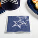 A blue and white Dallas Cowboys beverage napkin with stars on it next to a plate of food.
