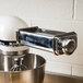 A KitchenAid stand mixer with a silver pasta roller attachment.