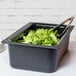 A Carlisle black plastic food pan filled with lettuce on a table in a salad bar.