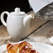 A white Villeroy & Boch porcelain teapot lid on a table with a croissant.