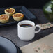 A white Villeroy & Boch porcelain stackable cup filled with brown liquid sits on a table with small pastries.