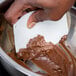 A person using an Ateco plastic bowl scraper to mix chocolate frosting in a bowl.