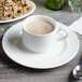 A Villeroy & Boch white porcelain cup of coffee on a saucer with food.