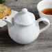 A white Villeroy & Boch teapot with a cup of tea on a saucer and a cookie.