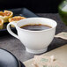 A white Villeroy & Boch porcelain cup of coffee on a saucer with small pastries.