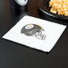 A Pittsburgh Steelers luncheon napkin with a football helmet on it on a table with a plate of food.