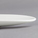 A white porcelain Villeroy & Boch gourmet boat plate with a curved edge on a gray surface.