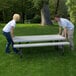A man and woman setting up a white Lifetime rectangular picnic table on grass.