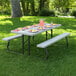 A Lifetime rectangular putty plastic picnic table with attached benches in a park with plates of food and drinks.