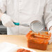 A person in a white coat using a Vollrath teal perforated oval spoodle to serve food.