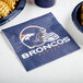 A blue Denver Broncos luncheon napkin with a football helmet logo next to a plate of french fries.