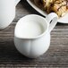 A white Villeroy & Boch porcelain creamer with a handle on a table with pastries.