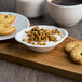 A Villeroy & Boch white porcelain oval bowl filled with granola and yogurt on a wood board with cookies and a cup of coffee.