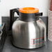 An orange and silver Choice insulated coffee carafe with a brew thru lid on a counter.