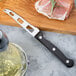 A Franmara serrated stainless steel cheese knife on a cutting board next to a glass of wine.