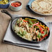 A Choice oval cast iron fajita skillet with chicken, rice, and vegetables on a table with tortillas and salsa.