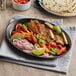 A Choice oval cast iron fajita skillet with sliced vegetables and tortillas on a table.