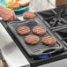 A person cooking hamburger patties on a Choice cast iron grill pan.